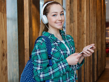 A 20-something white woman smiling while listening to music through headphones. An example of a 20 year old who chooses a nurse-midwife for her well-woman, sexual and reproductive healthcare in Connecticut.