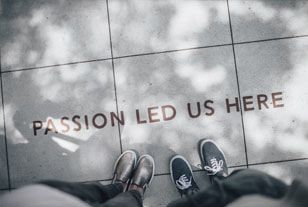 Legs and feet of two people looking down at the words 'Passion led us here' painted on a sidewalk. Represents the Purpose of Magnolia Midwifery.